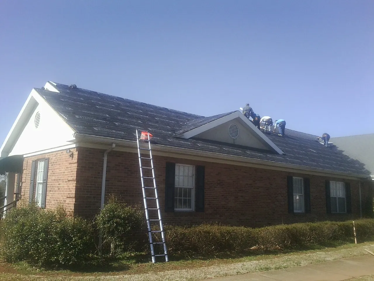 Crew tearing shingles off a brick ranch roof with a ladder set — Metal Roof Repair work by our crew in Patterson