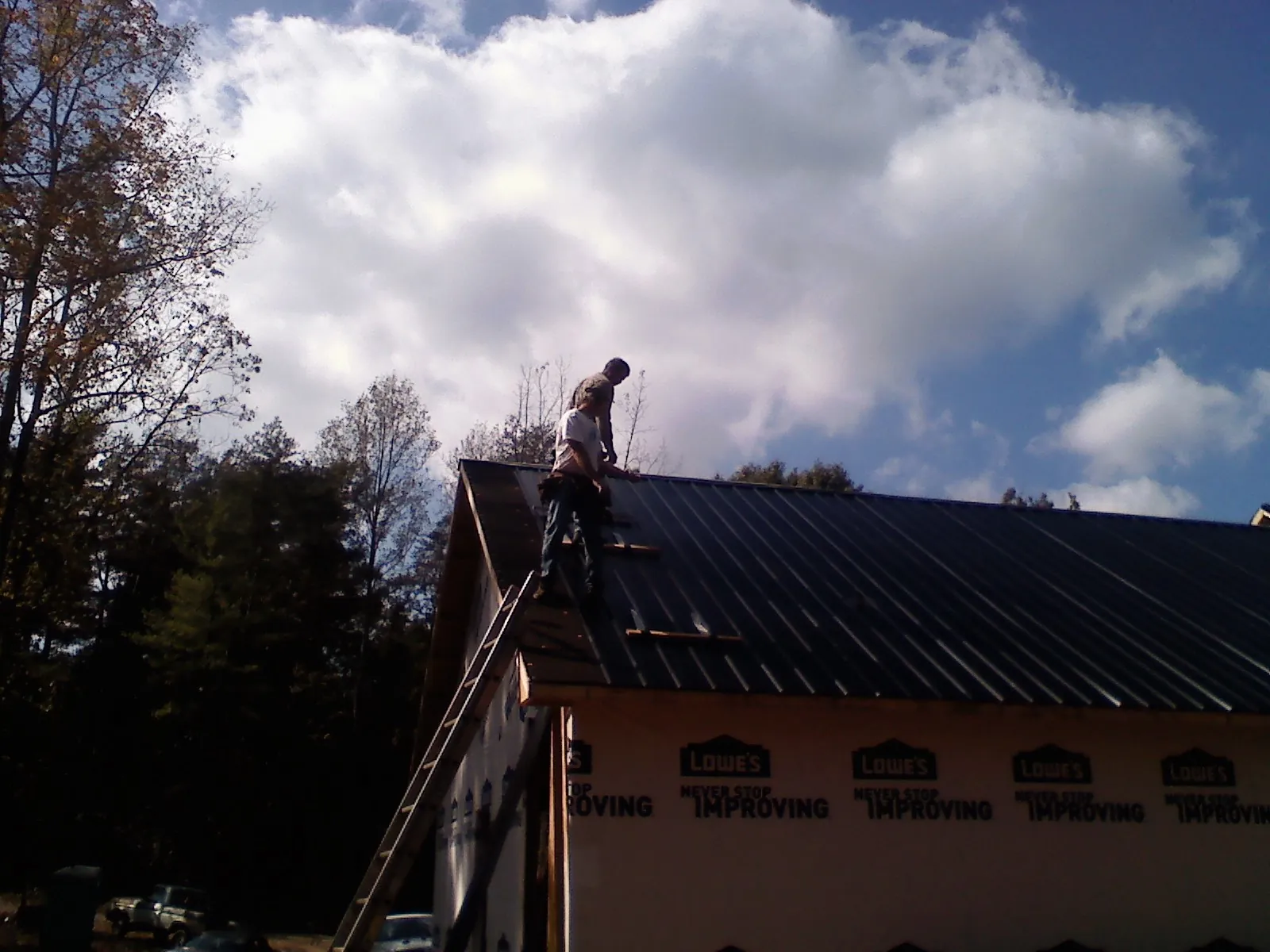Roofer fastening dark metal panels high against a cloudy sky, from a Roof Inspection job in Patterson